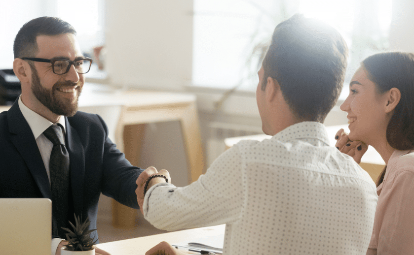 Business advisor shaking hands with young couple in office