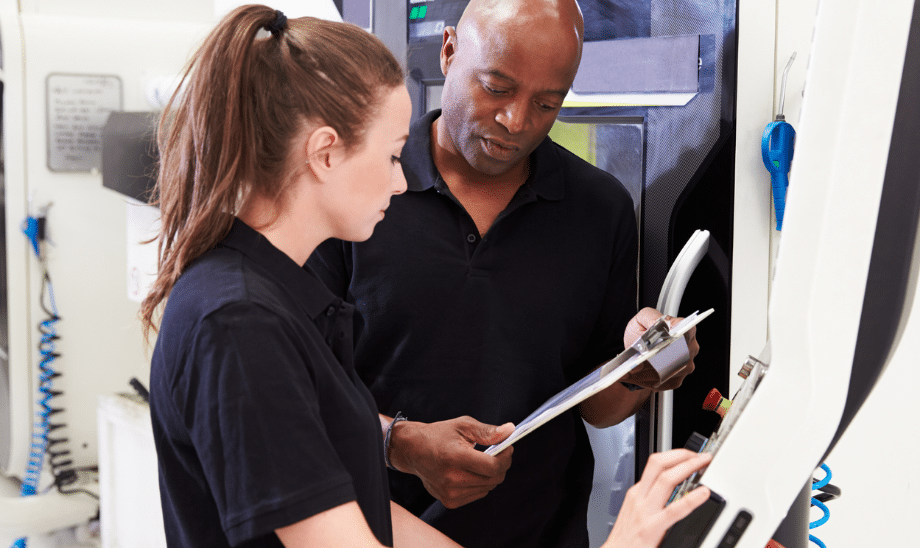 Experienced technician reviewing machine operation checklist with a young apprentice in a modern manufacturing environment